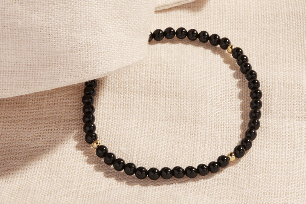 Black onyx and 14kt gold beaded bracelet on a linen background 